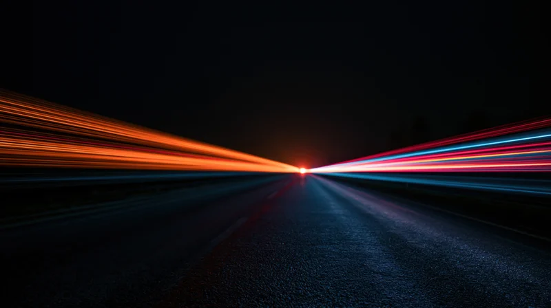 Long exposure view of a dark road with streaking vehicle lights converging toward a distant point