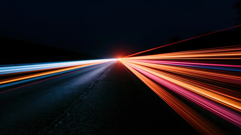 Long exposure view of a dark road with colorful light streaks from moving vehicles converging into the distance