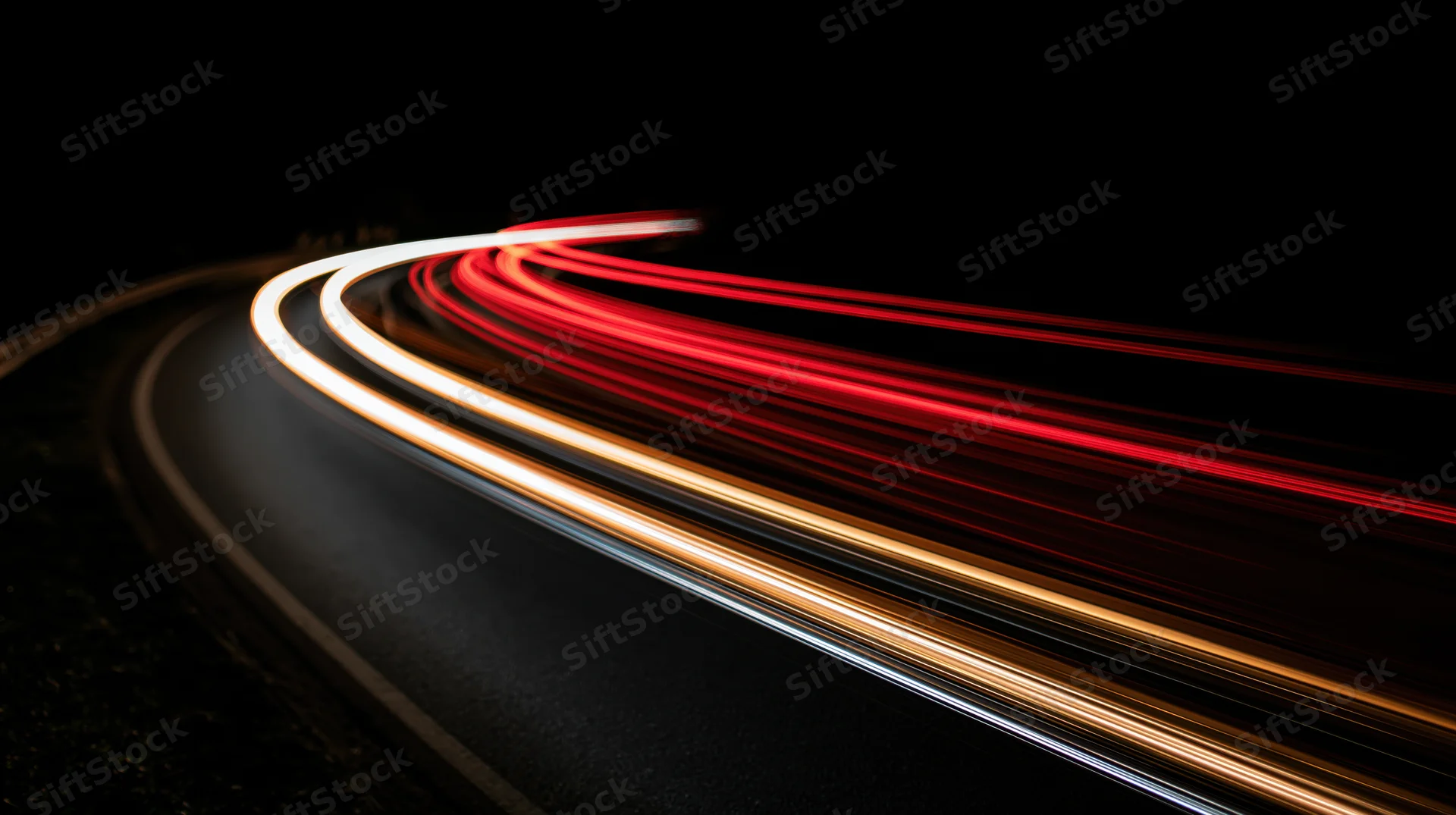 Curved road at night with light trails from moving vehicles