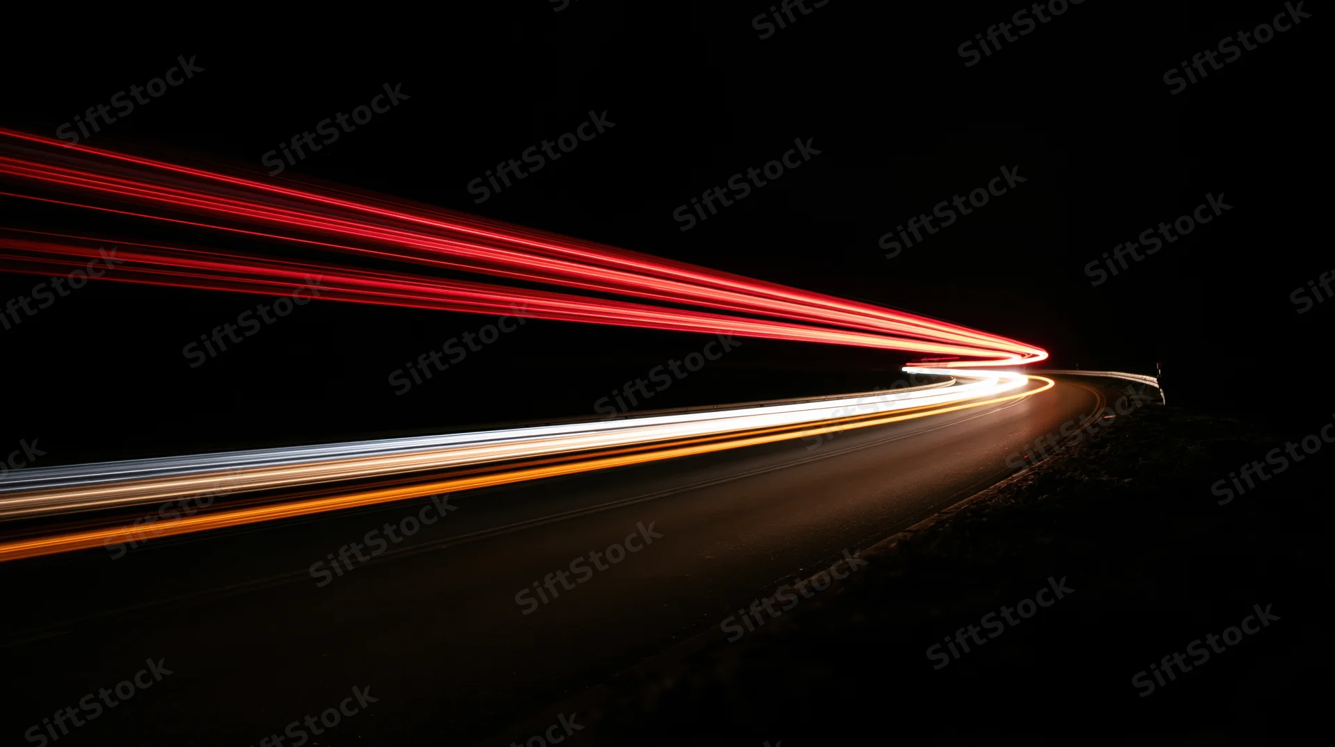Light trails from moving vehicles on a curving road at night