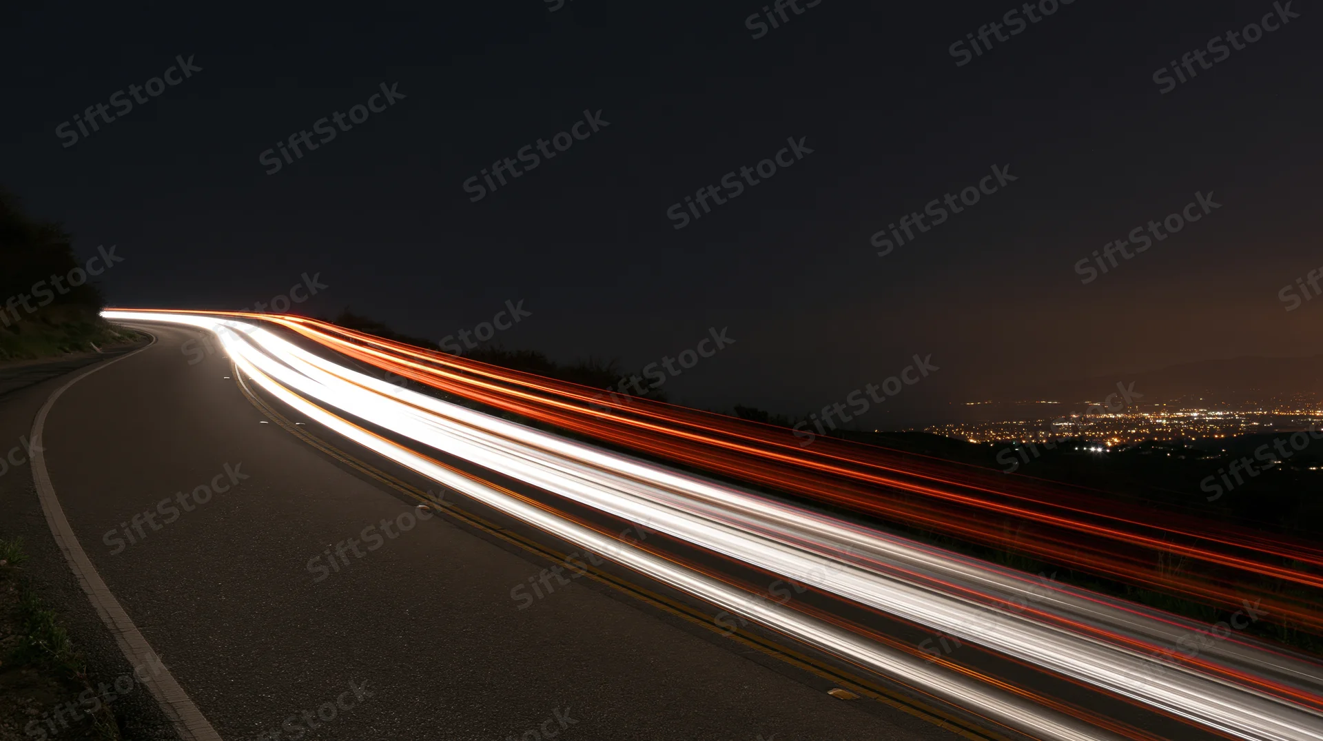 Light trails from moving vehicles on a winding highway at night overlooking a cityscape