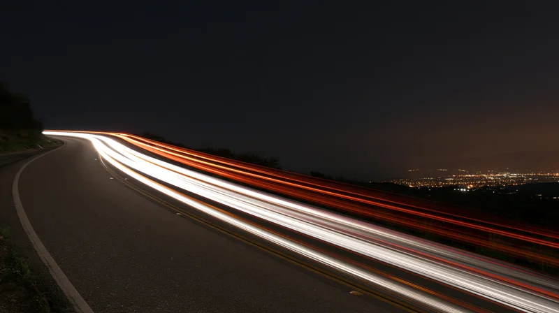 Light trails from moving vehicles on a winding highway at night overlooking a cityscape