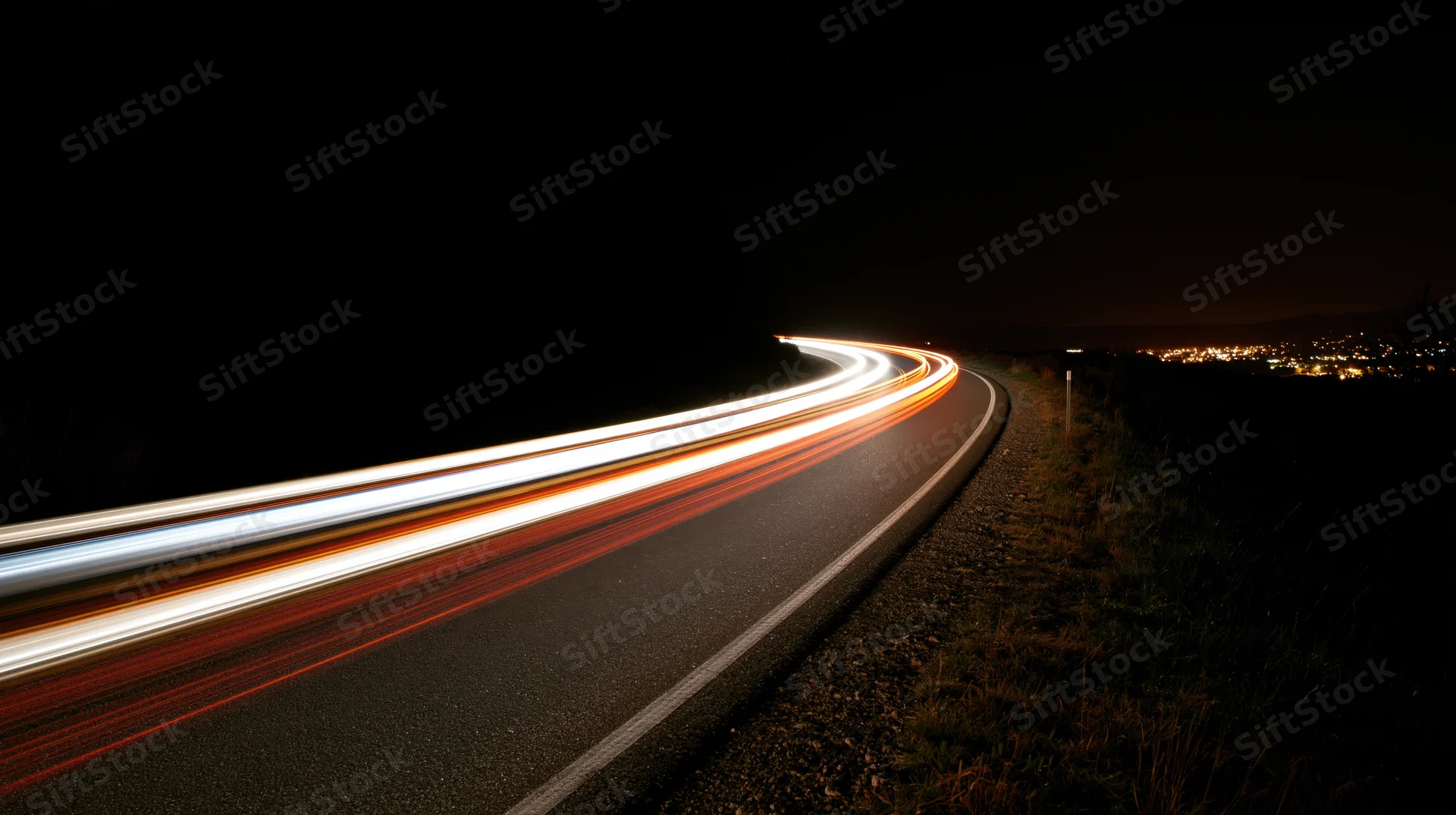 Winding road at night with light trails from moving vehicles curving into the distance