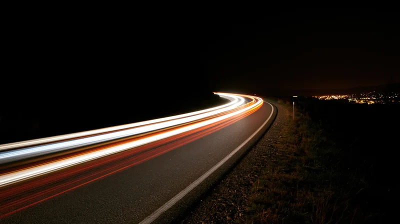 Winding road at night with light trails from moving vehicles curving into the distance