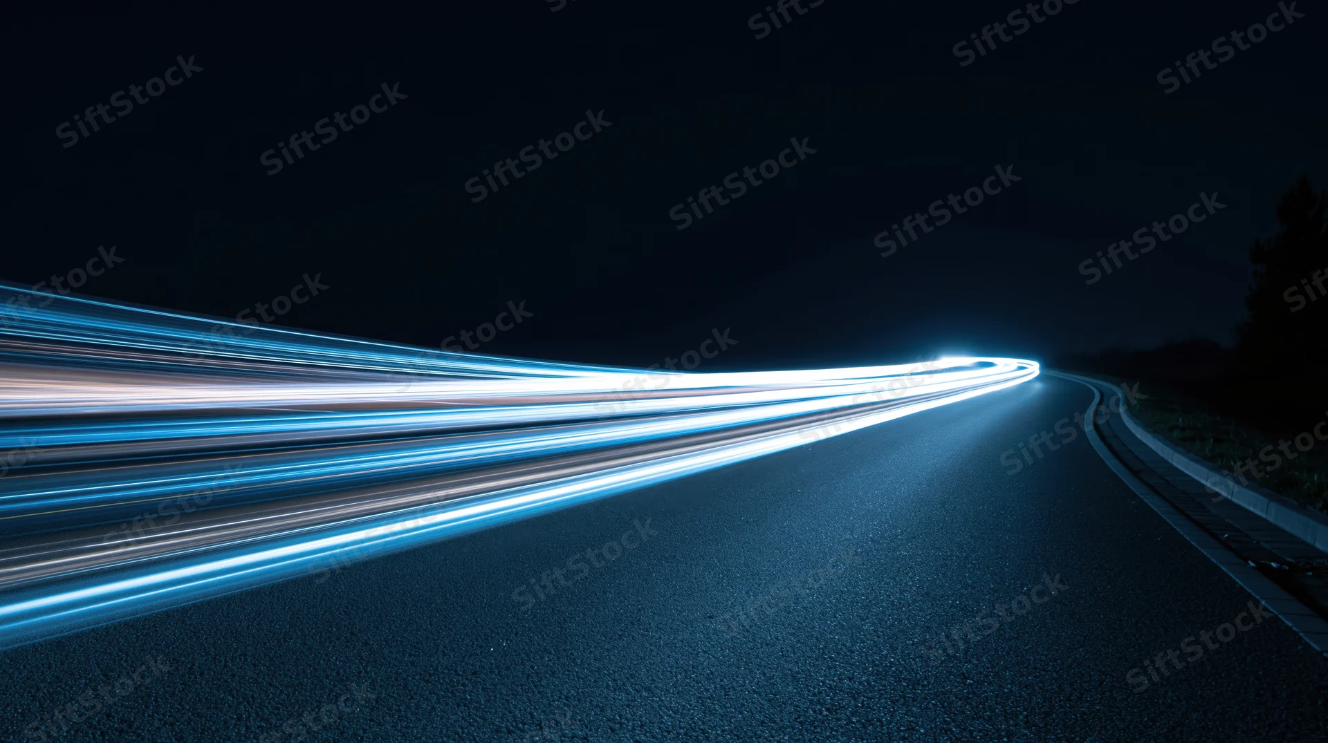 Curved asphalt road at night with light streaks from moving vehicles