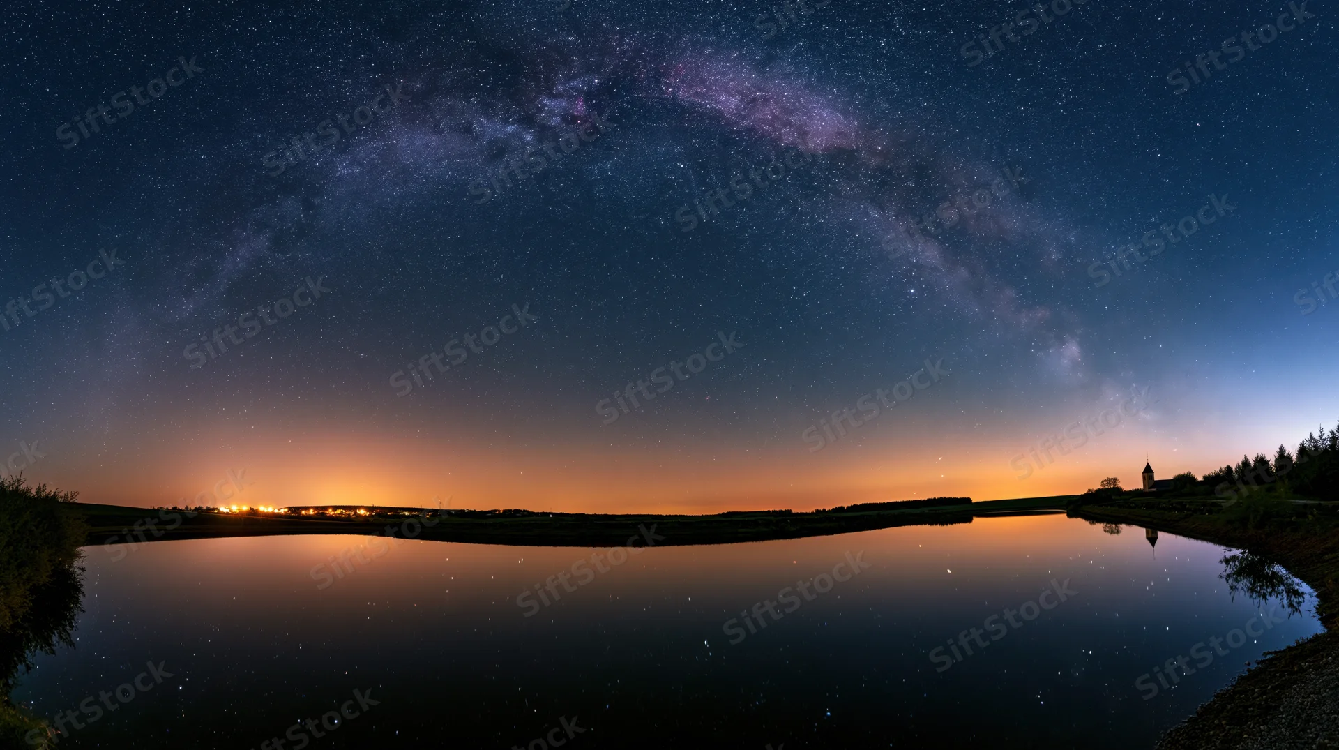 Milky way reflected in calm lake water at night under dark sky with distant horizon glow