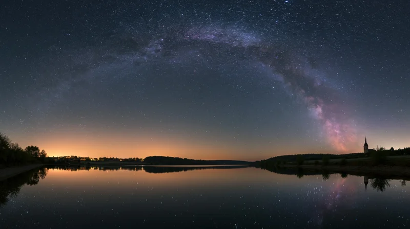 Milky way arching over calm lake reflecting stars and distant church steeple at twilight