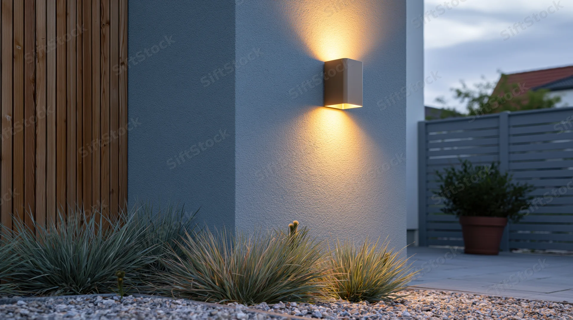 Modern outdoor wall sconce illuminating a garden bed beside a patio at dusk