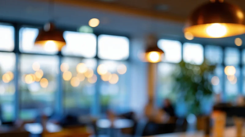 Blurred interior of a modern restaurant with warm pendant lights and large windows, showing tables and chairs in soft focus