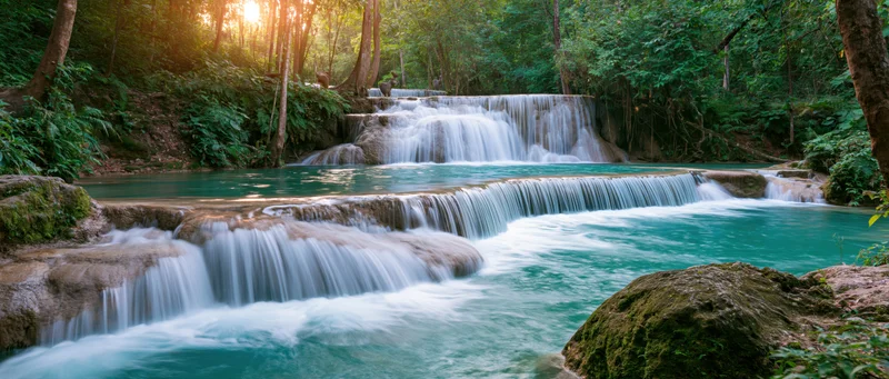 Cascading waterfall flowing over mossy rocks in a lush green forest at sunrise