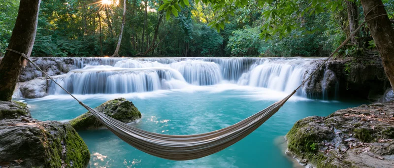 Hammock suspended between trees over a turquoise river with cascading waterfall in a lush jungle setting