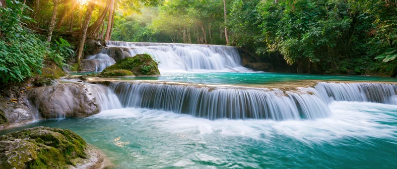 Cascading waterfall flowing over mossy rocks in a lush tropical forest at sunrise