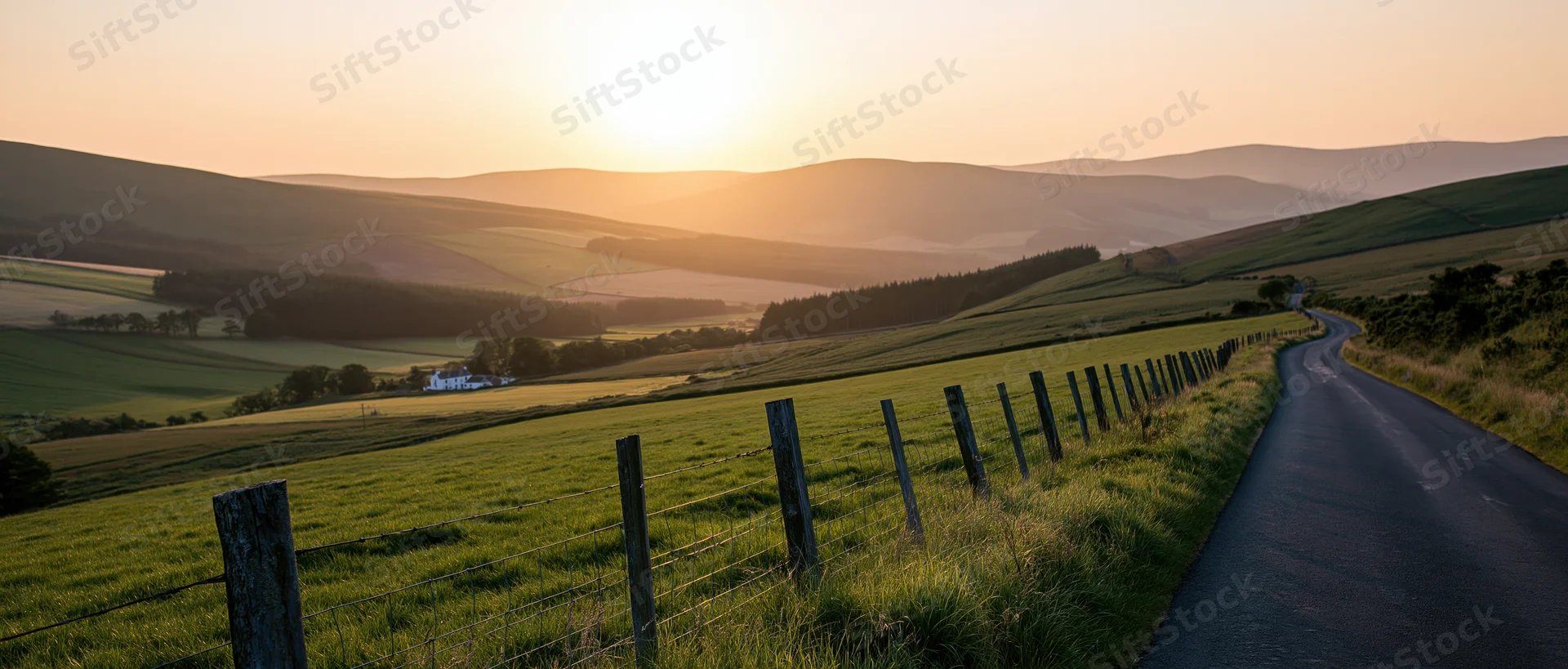 Winding asphalt road through green fields and rolling hills at sunset