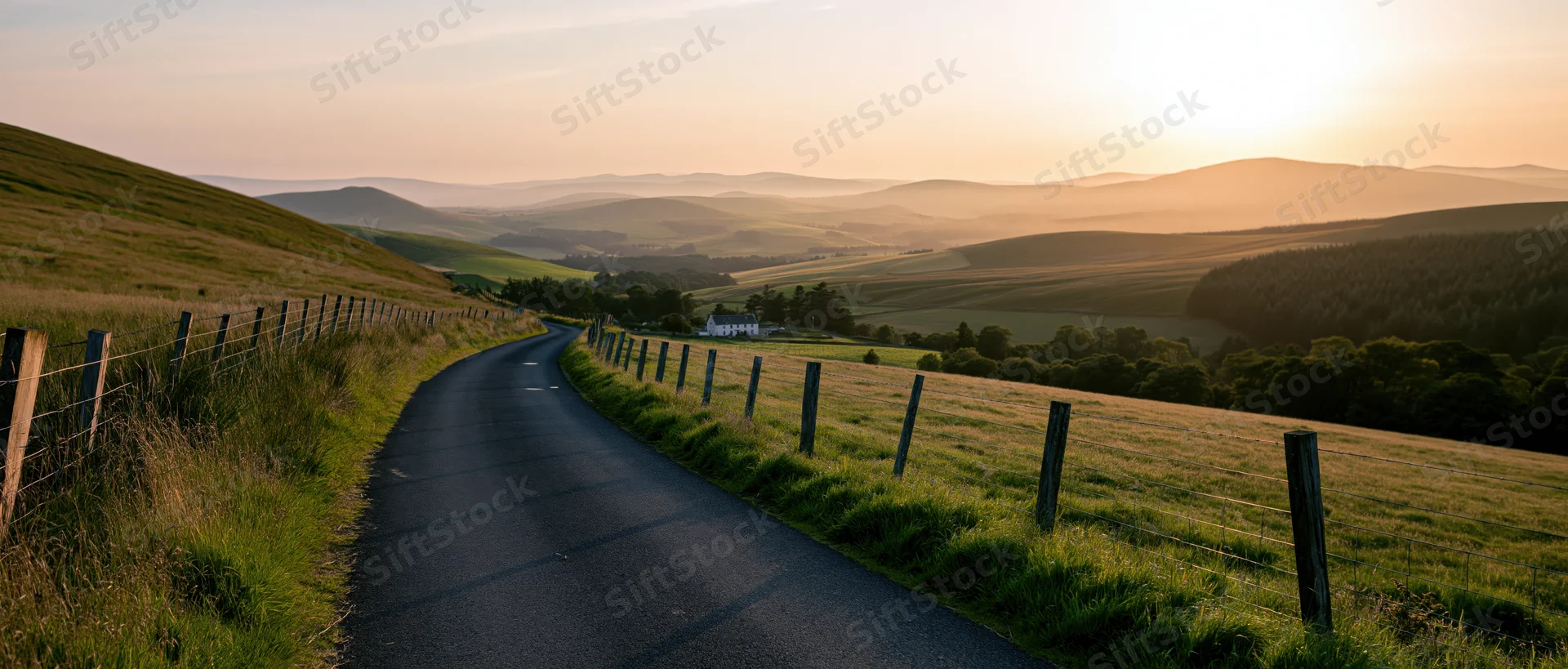 Winding asphalt road through grassy hills at sunset in the Scottish countryside