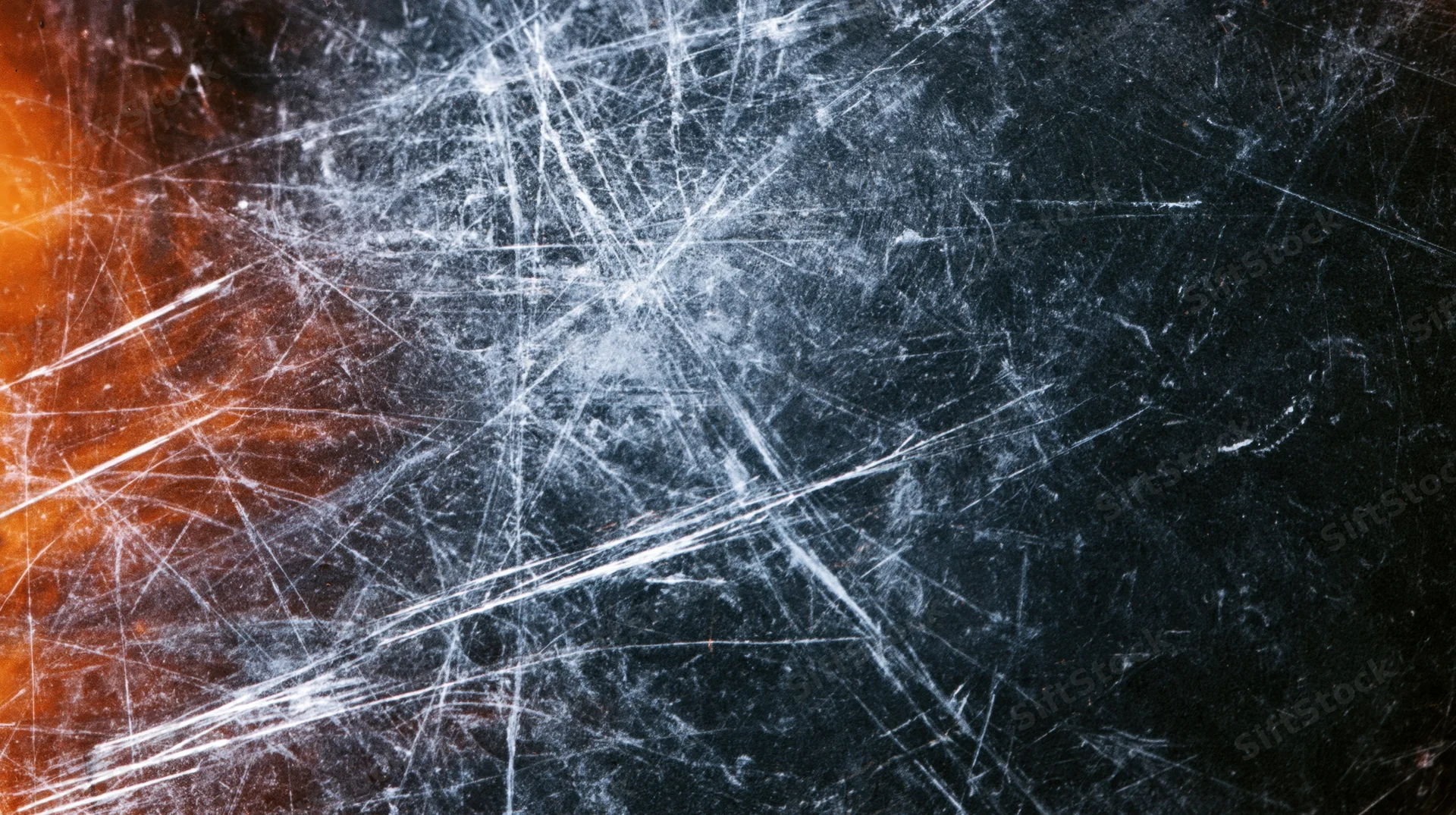Scratched glass surface with intersecting white lines and orange glow on dark background