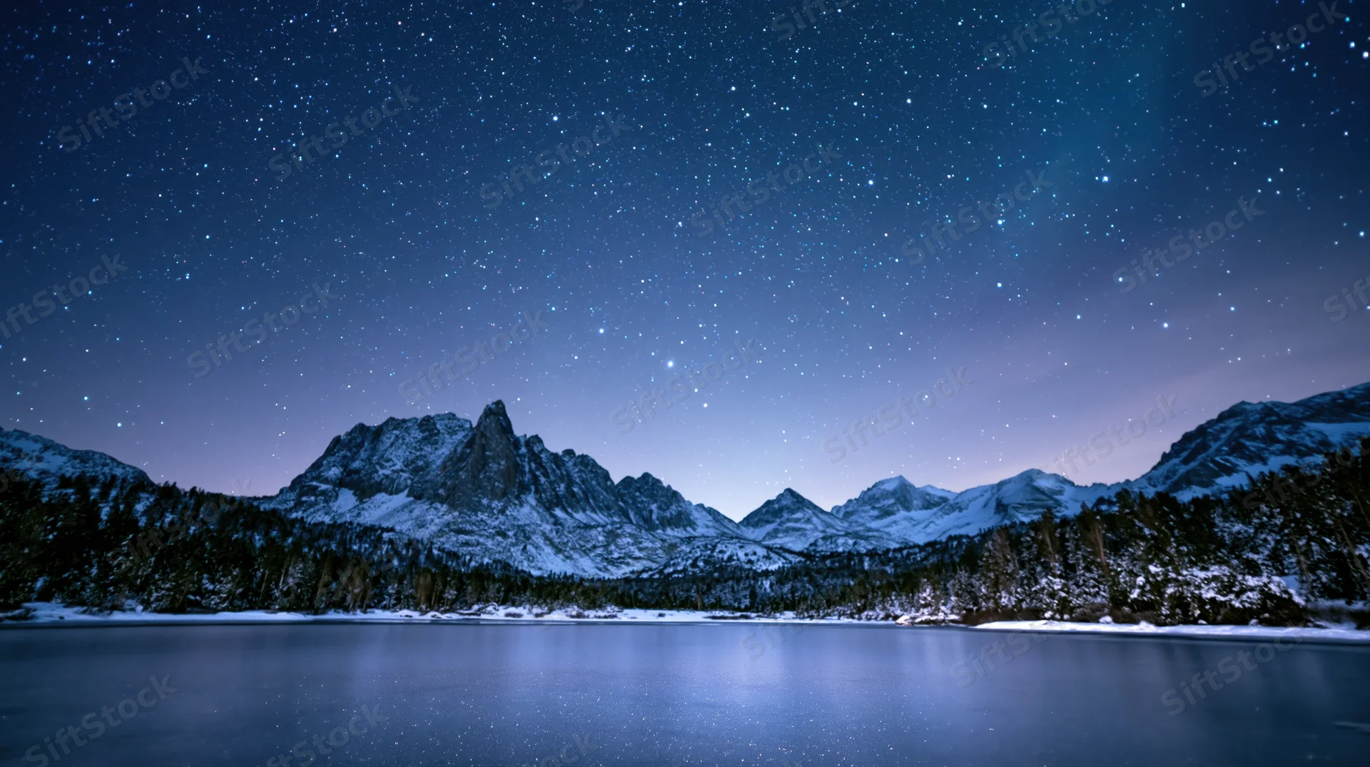 Snow-covered mountains reflected in a frozen lake under a star-filled night sky