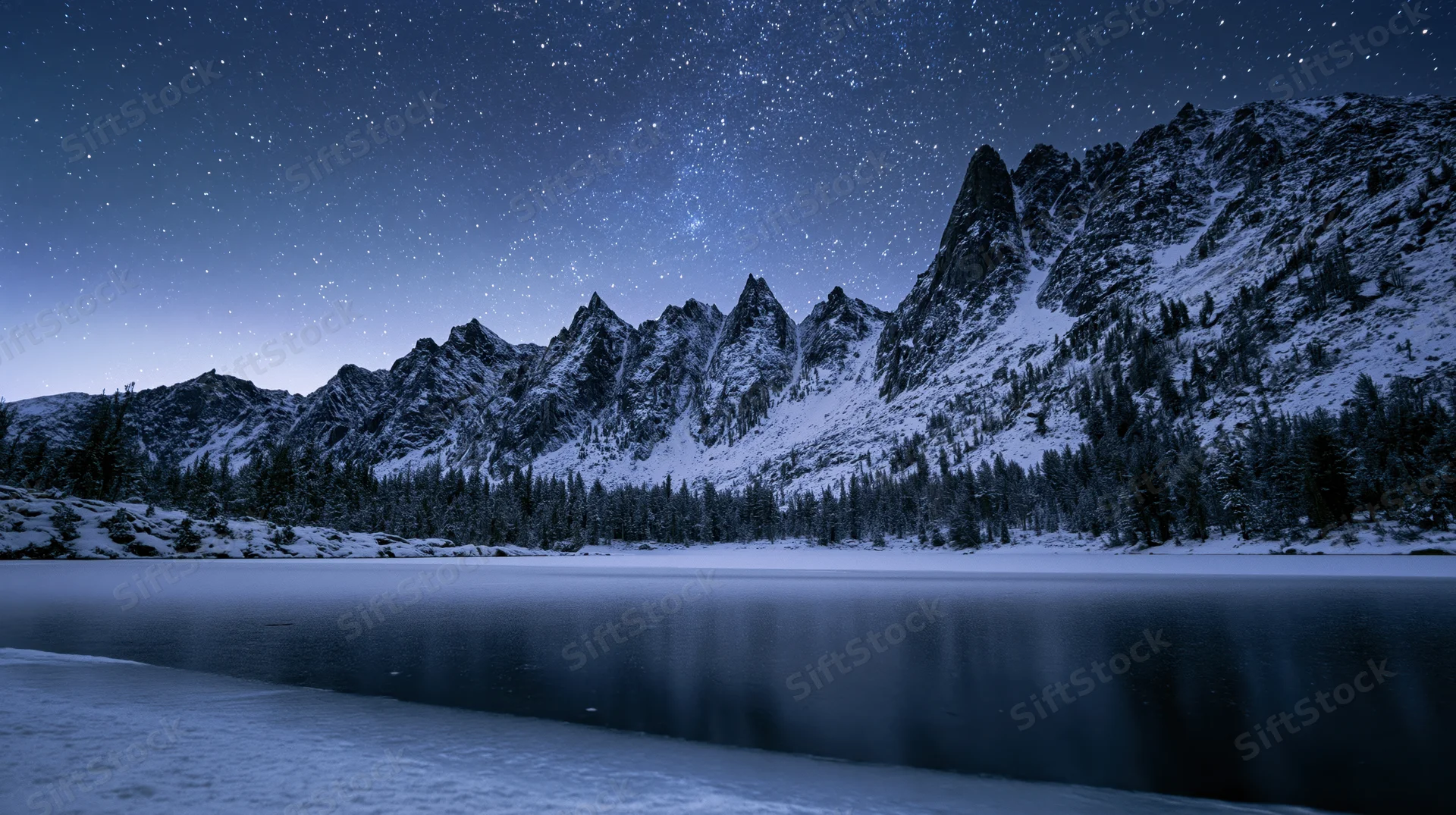 Snow-covered mountain peaks reflected in a frozen lake under a starry night sky