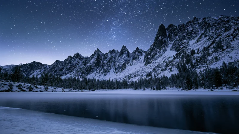 Snow-covered mountain peaks reflected in a frozen lake under a starry night sky