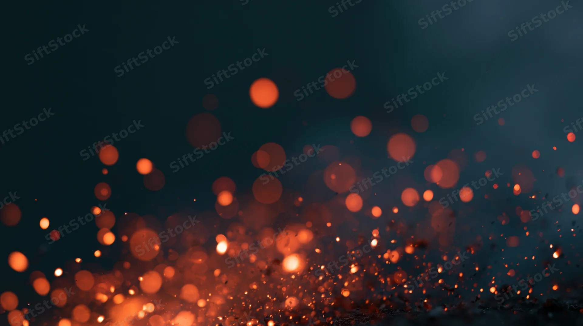 Glowing orange sparks rising in a dark space with blurred bokeh effect