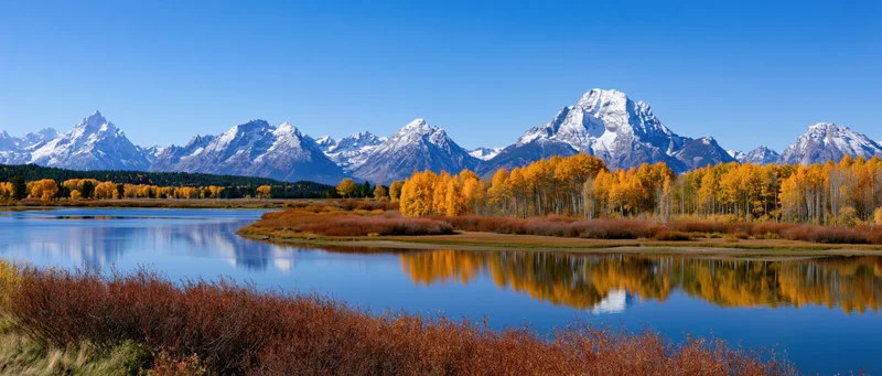 Snow-capped mountains reflected in a calm lake surrounded by autumn aspen trees in a valley