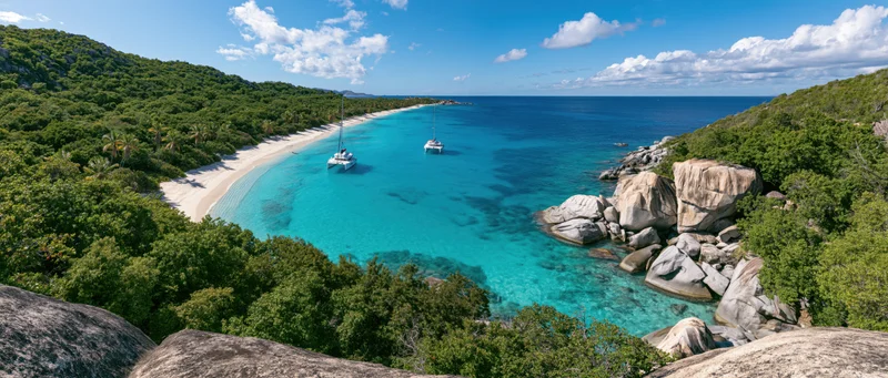 Turquoise water in a tropical bay surrounded by green hills and rocks with sailboats anchored near the shore