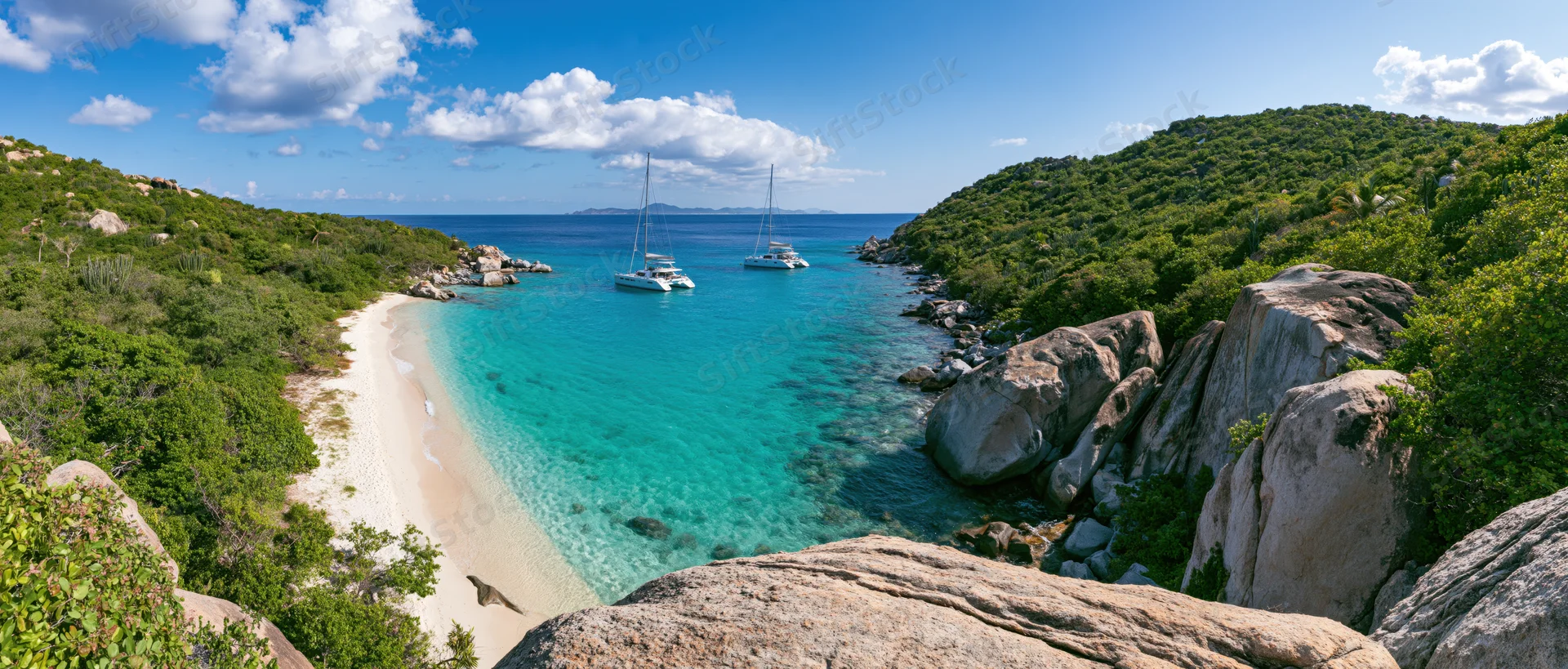 Two catamarans anchored in a turquoise cove surrounded by green hills and rocky shores