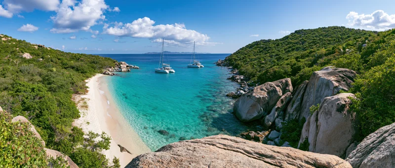 Two catamarans anchored in a turquoise cove surrounded by green hills and rocky shores