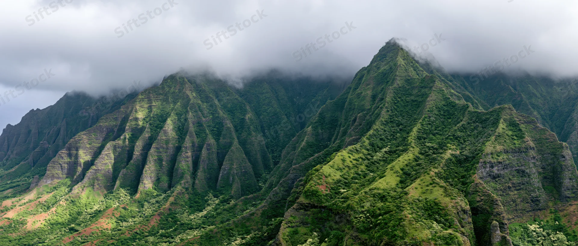 Rugged green mountain peaks rising from forested valleys under cloudy sky in hawaii