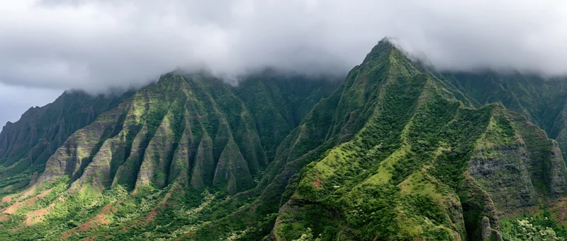 Rugged green mountain peaks rising from forested valleys under cloudy sky in hawaii