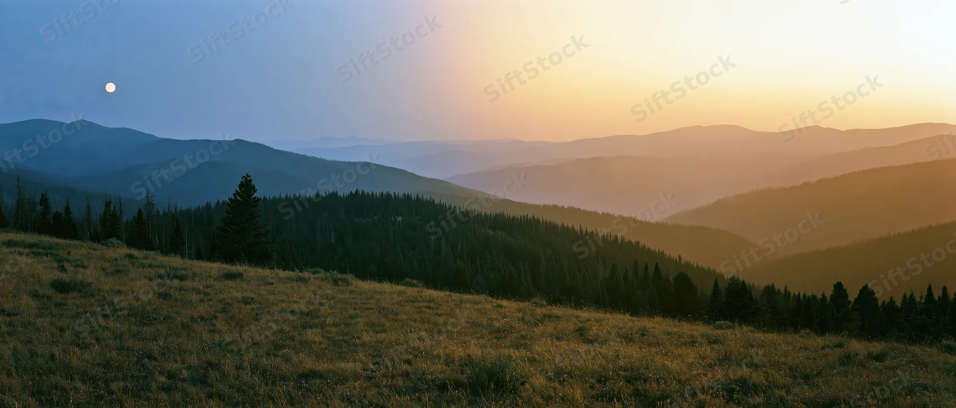 Mountain range at sunset with forested slopes and a visible moon in the sky