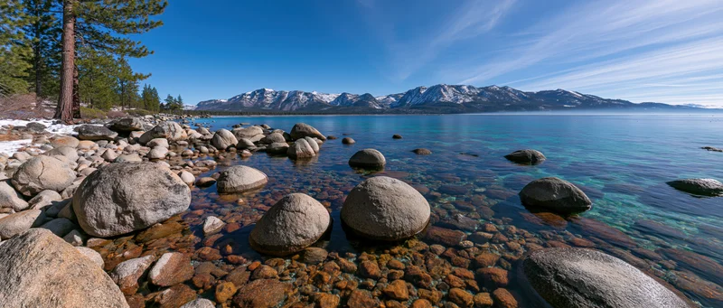 Clear turquoise lake with rocks and snow-capped mountains in the background