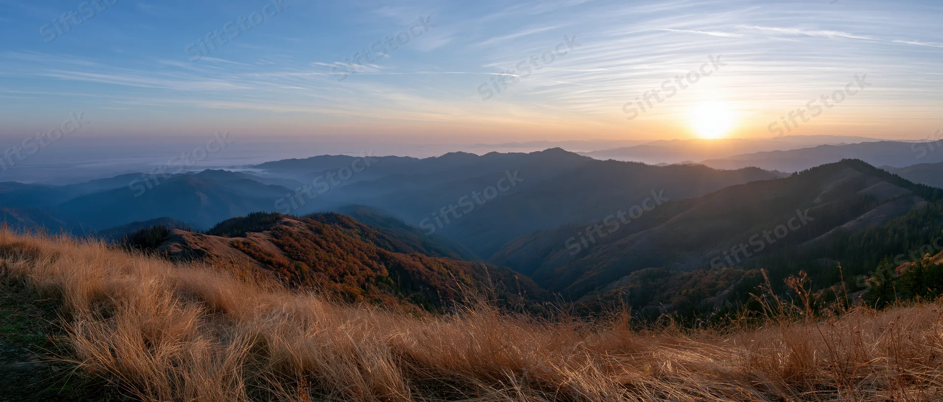 Sunrise over layered mountains and valleys with dry grass in foreground