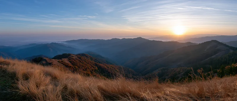 Sunrise over layered mountains and valleys with dry grass in foreground