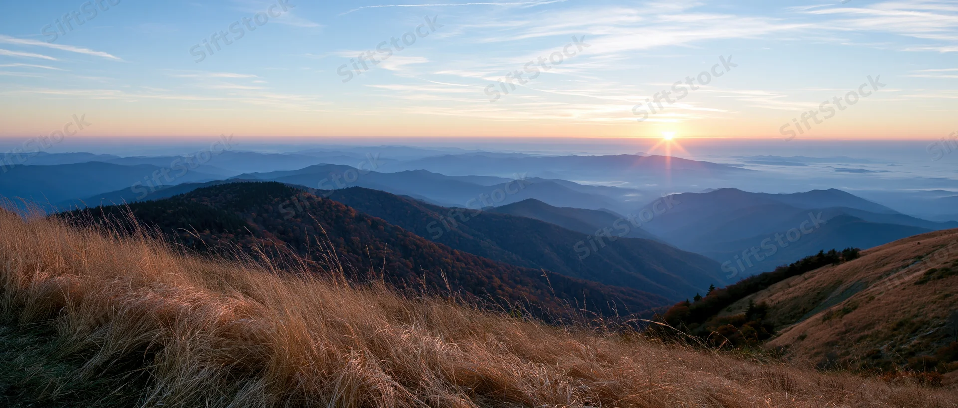 Sunrise over layered mountains and valleys with golden grass in foreground