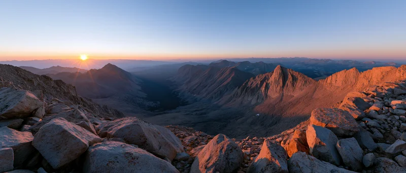 Sunrise over rugged mountain peaks and deep valley from high alpine summit