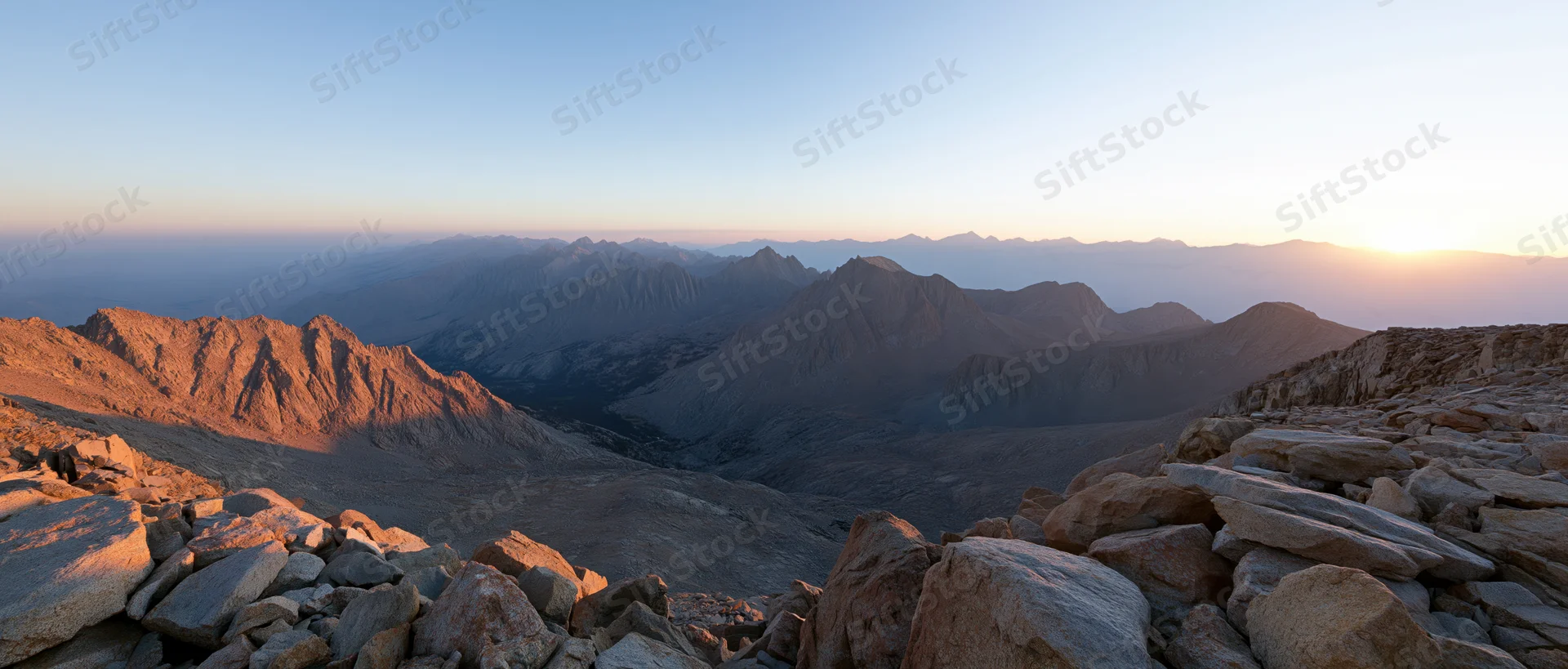 Rocky mountain ridge at sunrise overlooking a vast alpine valley