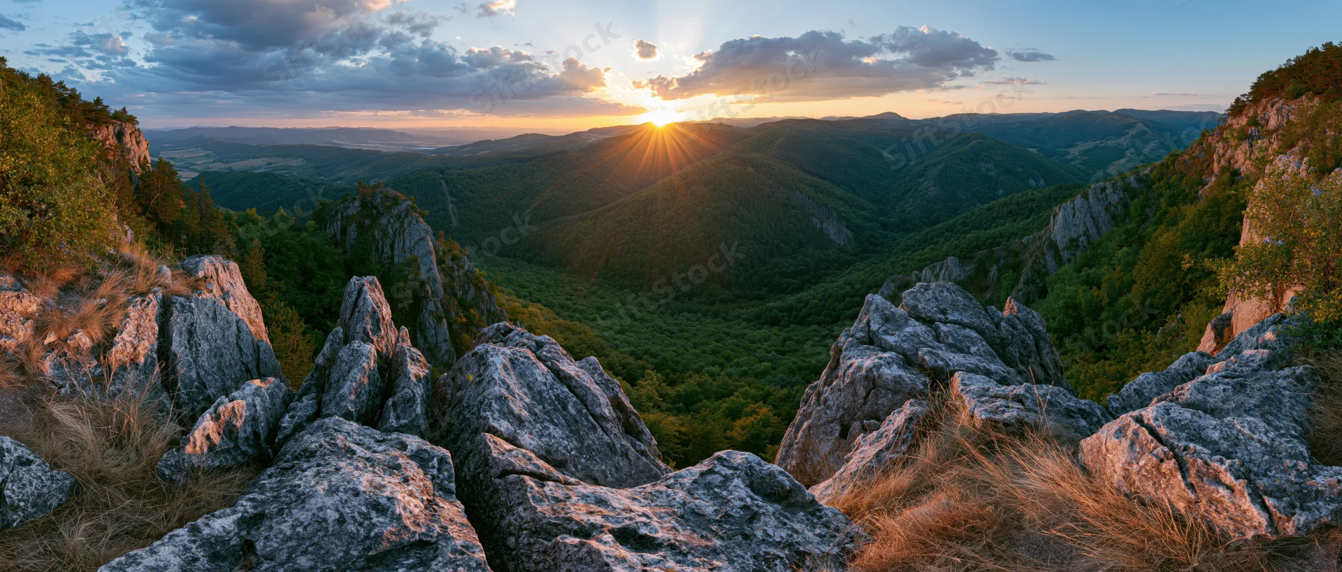 Sunset over a mountain valley with rocky outcrops and dense forest below