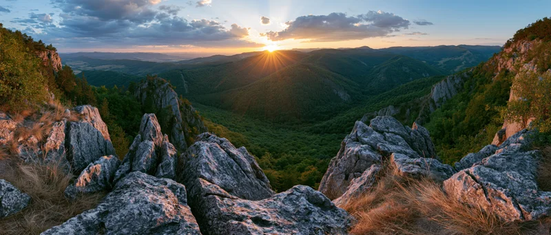 Sunset over a mountain valley with rocky outcrops and dense forest below