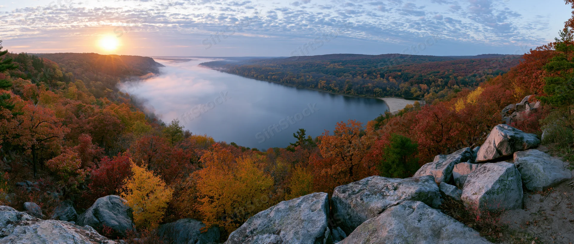 Autumn forest landscape with fog-covered lake at sunrise viewed from rocky overlook