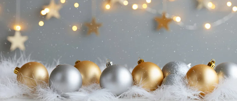 Gold and silver christmas ornaments arranged on white fluffy material with string lights and stars in background