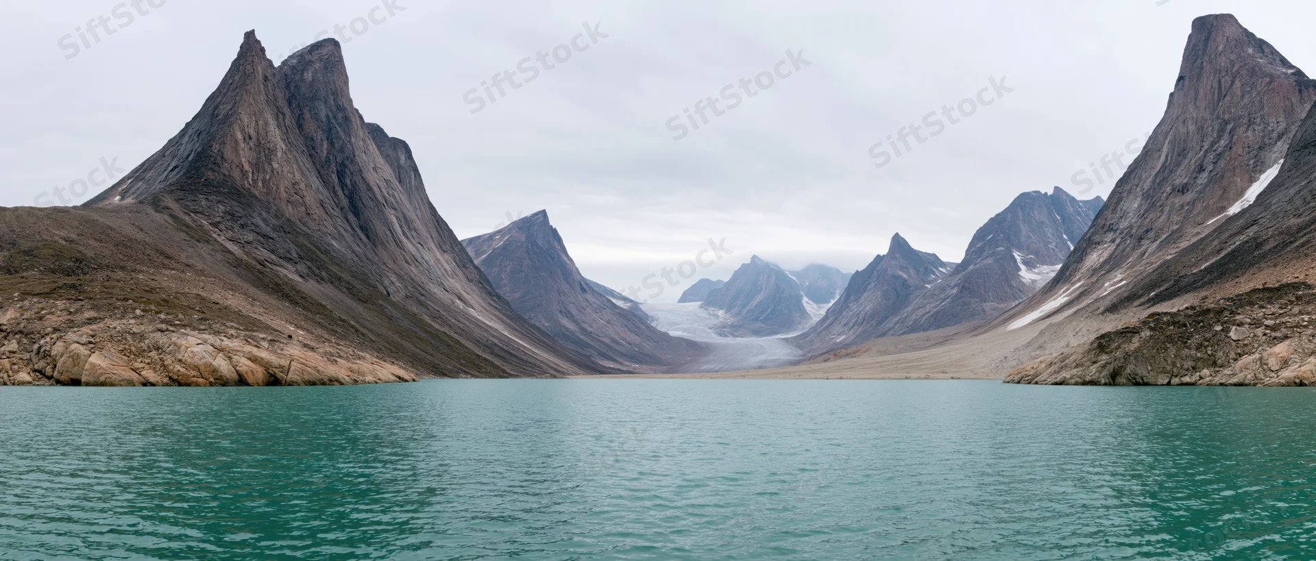 Turquoise lake surrounded by jagged alpine peaks and a distant glacier in a remote mountain valley