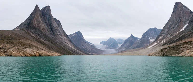 Turquoise lake surrounded by jagged alpine peaks and a distant glacier in a remote mountain valley