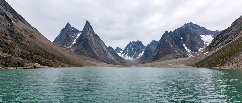 Alpine lake surrounded by jagged snow-dusted peaks under an overcast sky
