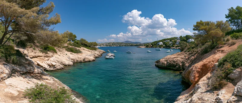 Turquoise water in a rocky cove with boats anchored near a coastal village under a blue sky with white clouds