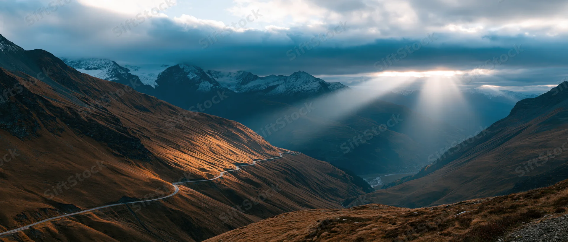 Winding road through mountain valley with sunlight breaking through clouds