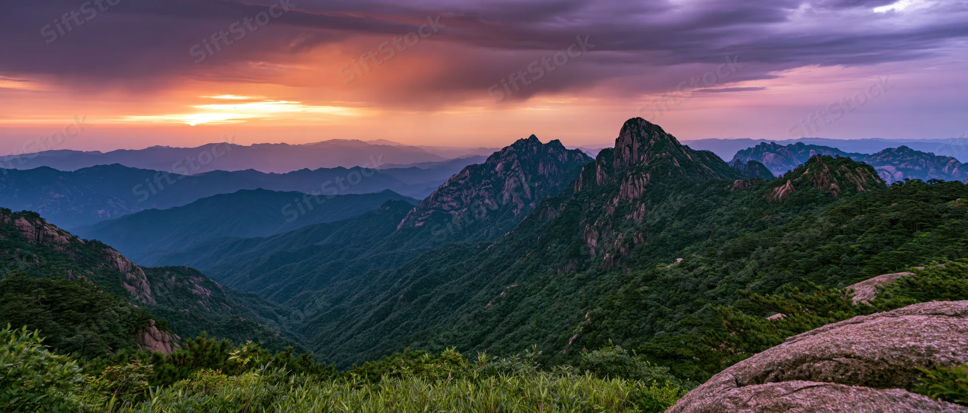 Mountain peaks rising over a forested valley at sunset
