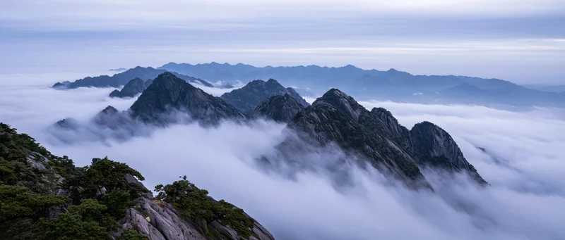 Rugged mountain peaks rising above a sea of clouds in a misty alpine landscape