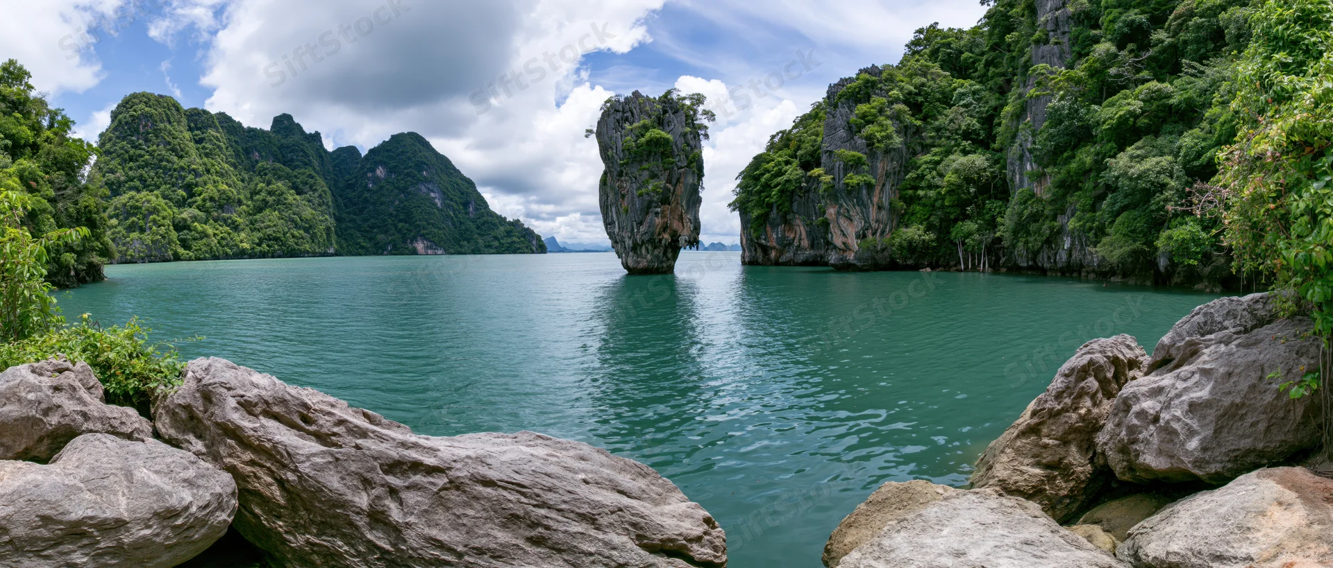 Limestone karst island rising from turquoise sea in tropical bay surrounded by forested cliffs