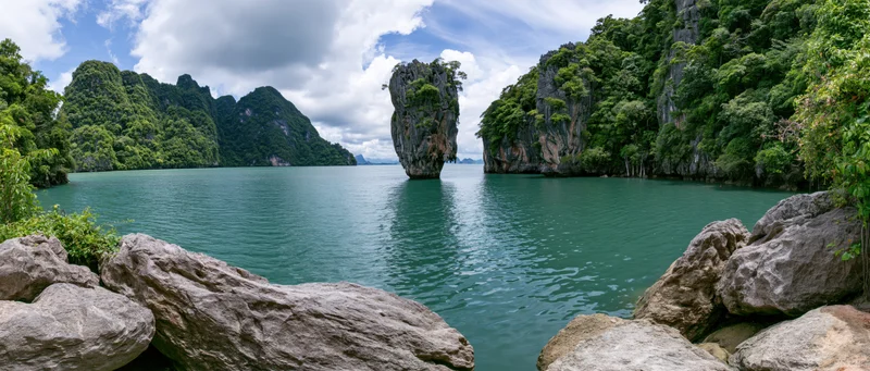Limestone karst island rising from turquoise sea in tropical bay surrounded by forested cliffs
