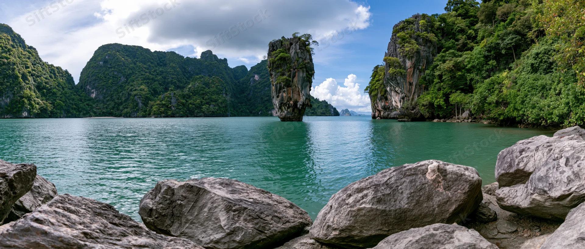 Limestone karst island rising from turquoise sea surrounded by jungle-covered cliffs in tropical bay